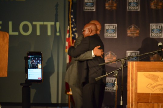 Ronnie Lott and father Roy Lott hug before reveling the Hall of Famer trophy